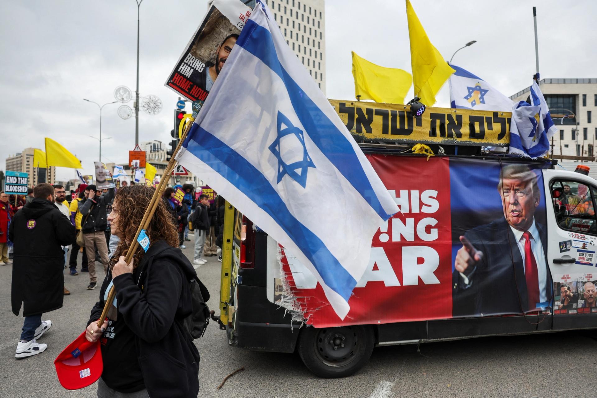 A woman carries an Israeli flag next to a banner with an image of U.S. President Donald Trump, during a demonstration calling for the immediate return of hostages held in Gaza, amid a ceasefire between Israel and Hamas, outside Prime Minister office in Jerusalem February 11, 2025.