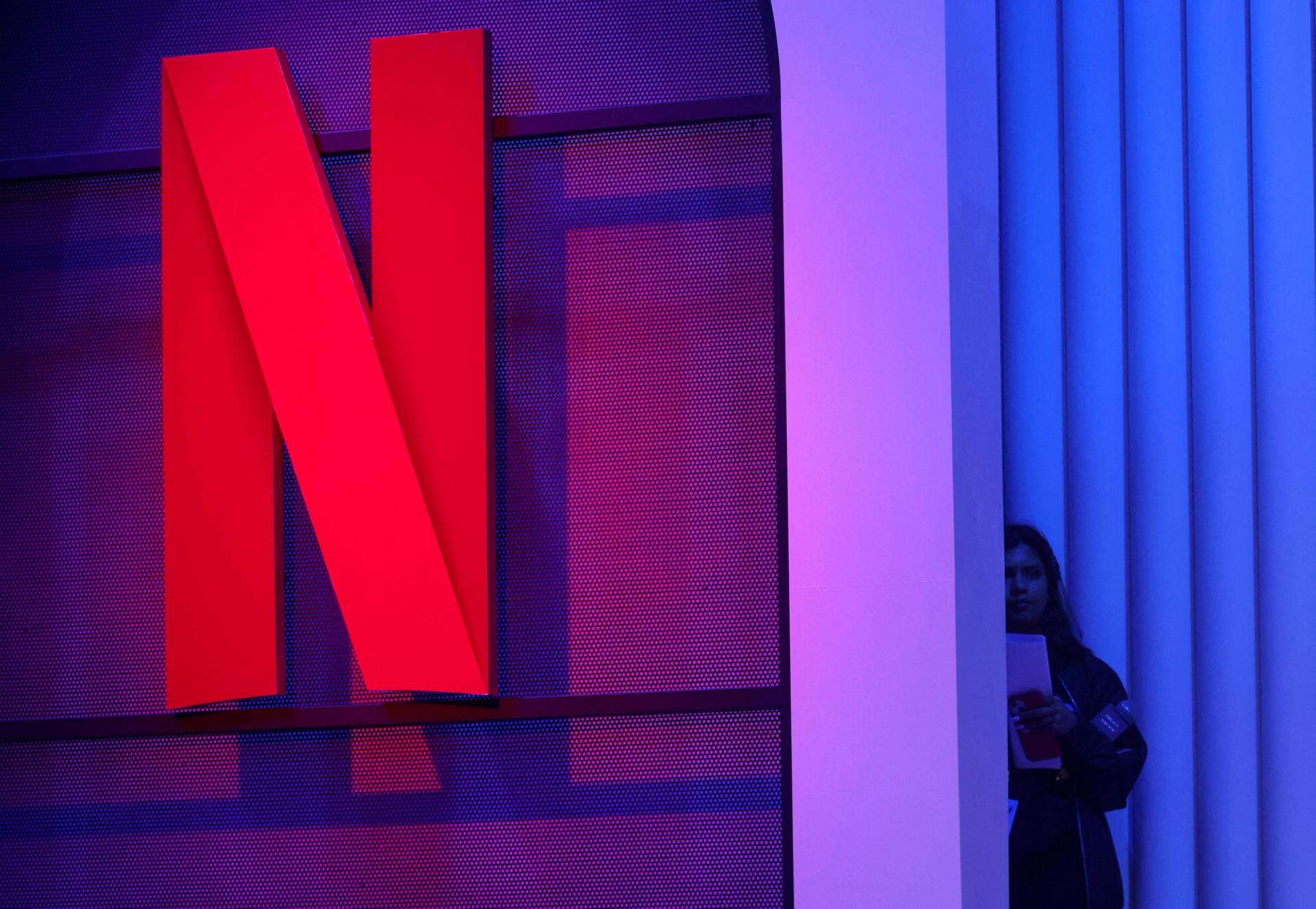 A woman stands next to a logo of Netflix during an event in Mumbai.