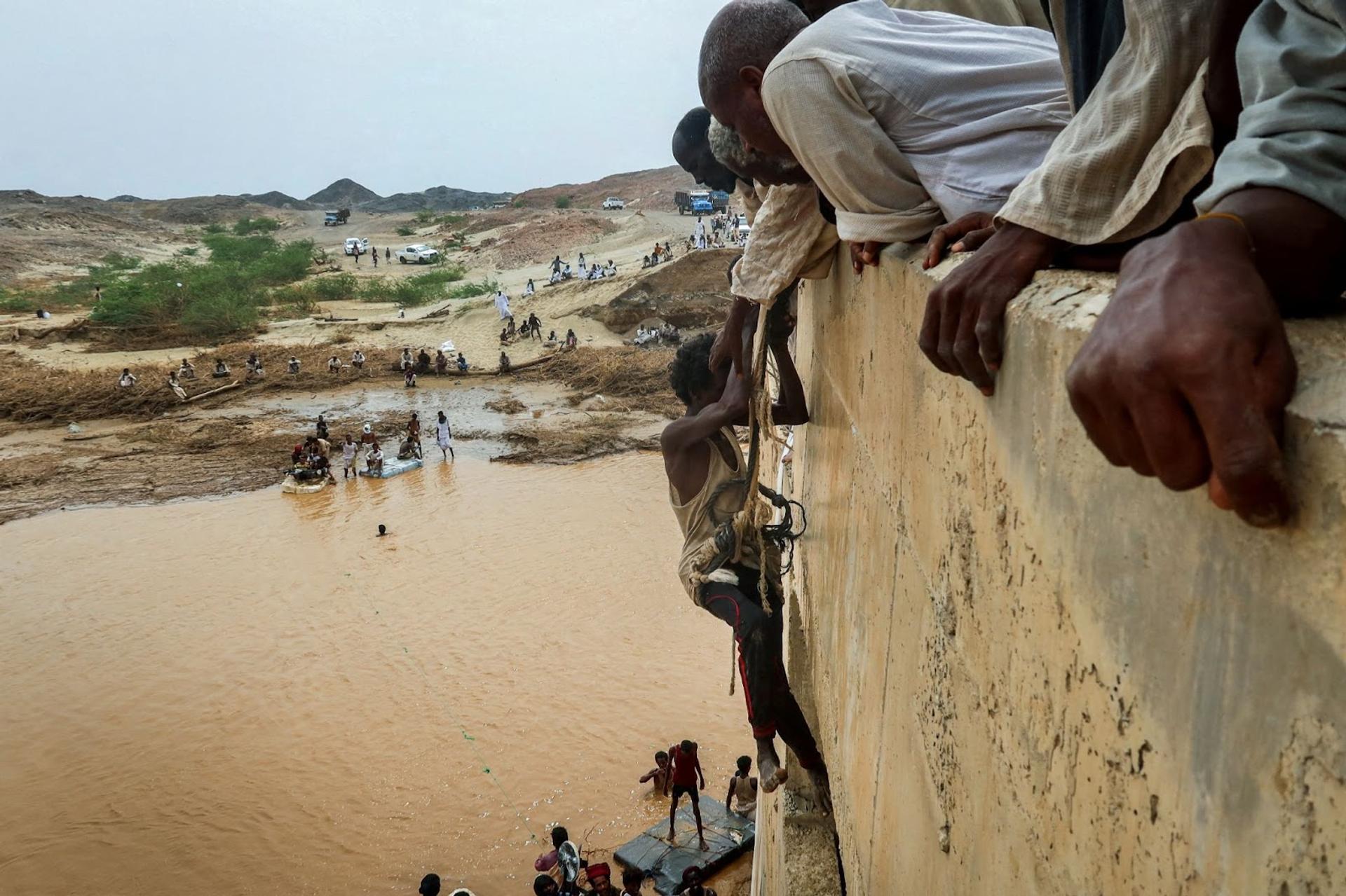 A survivor harnessed to a rope is helped to climb a wall following floods in Sudan.