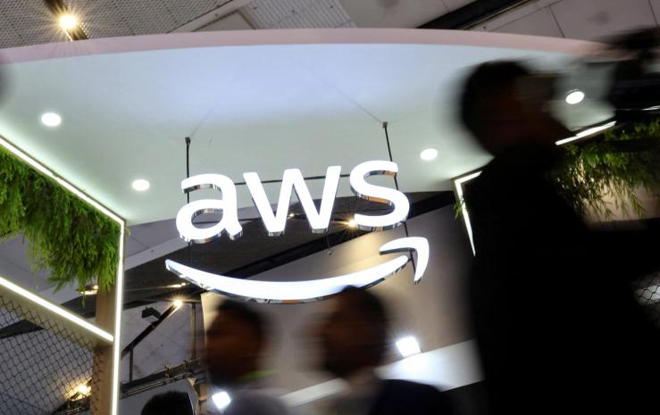 People walk past the logo of Amazon Web Services (AWS) at its exhibitor stall at the India Mobile Congress 2025