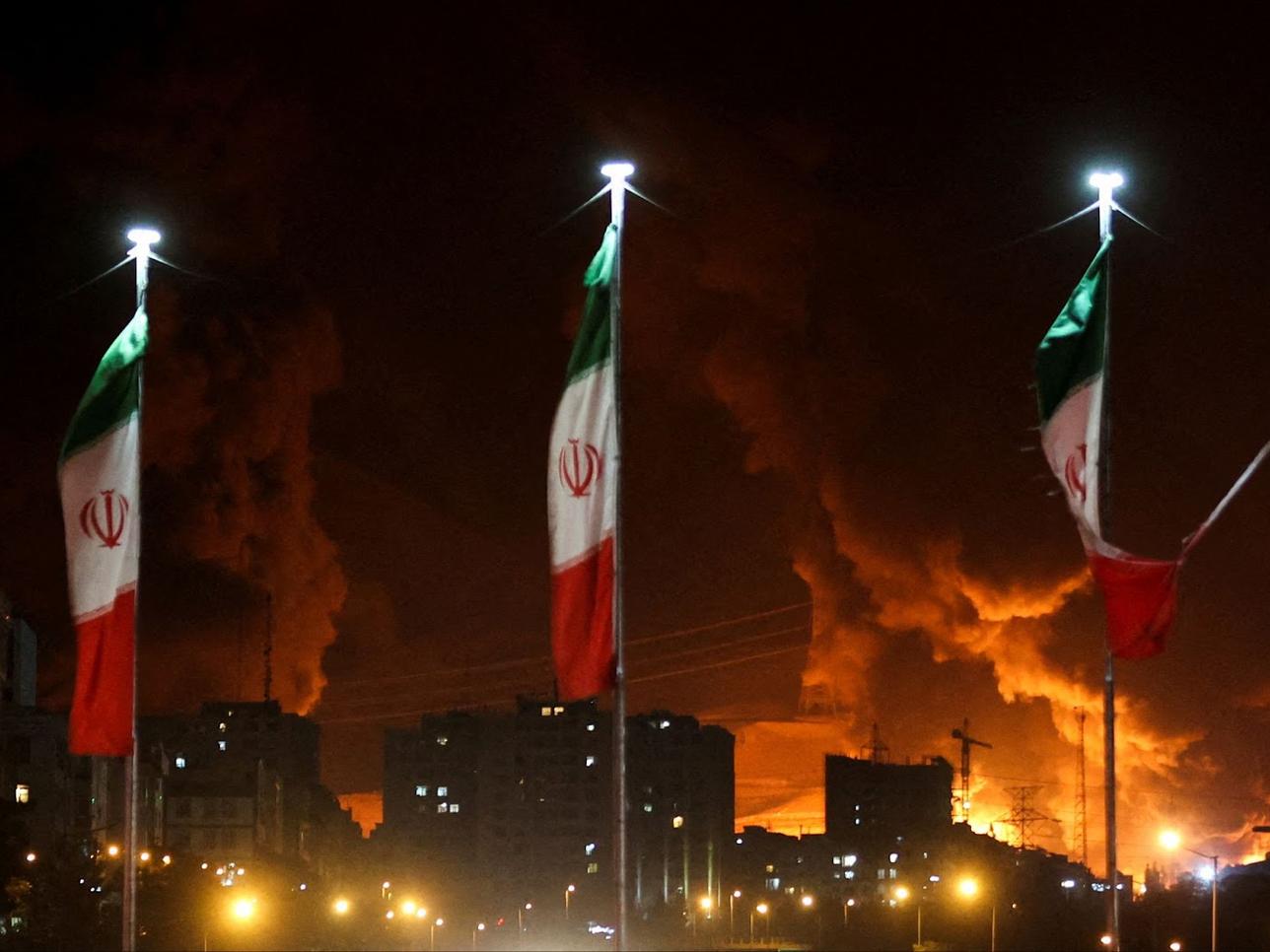 Iranian flags fly as fire and smoke from an Israeli attack on Sharan Oil depot rise, following Israeli strikes on Iran, in Tehran, Iran, June 15, 2025.