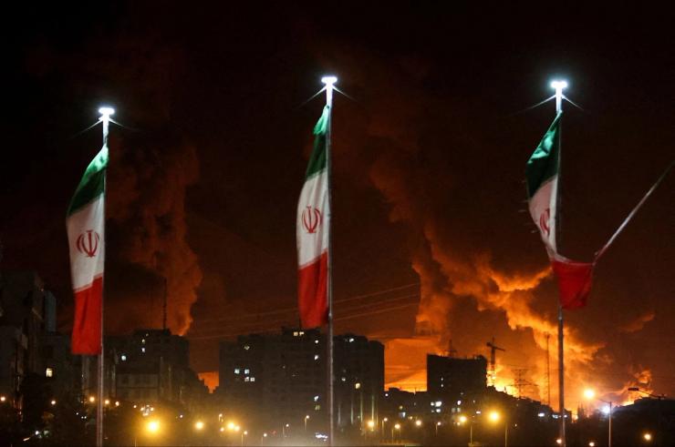 Iranian flags fly as fire and smoke from an Israeli attack on Sharan Oil depot rise, following Israeli strikes on Iran, in Tehran, Iran, June 15, 2025.