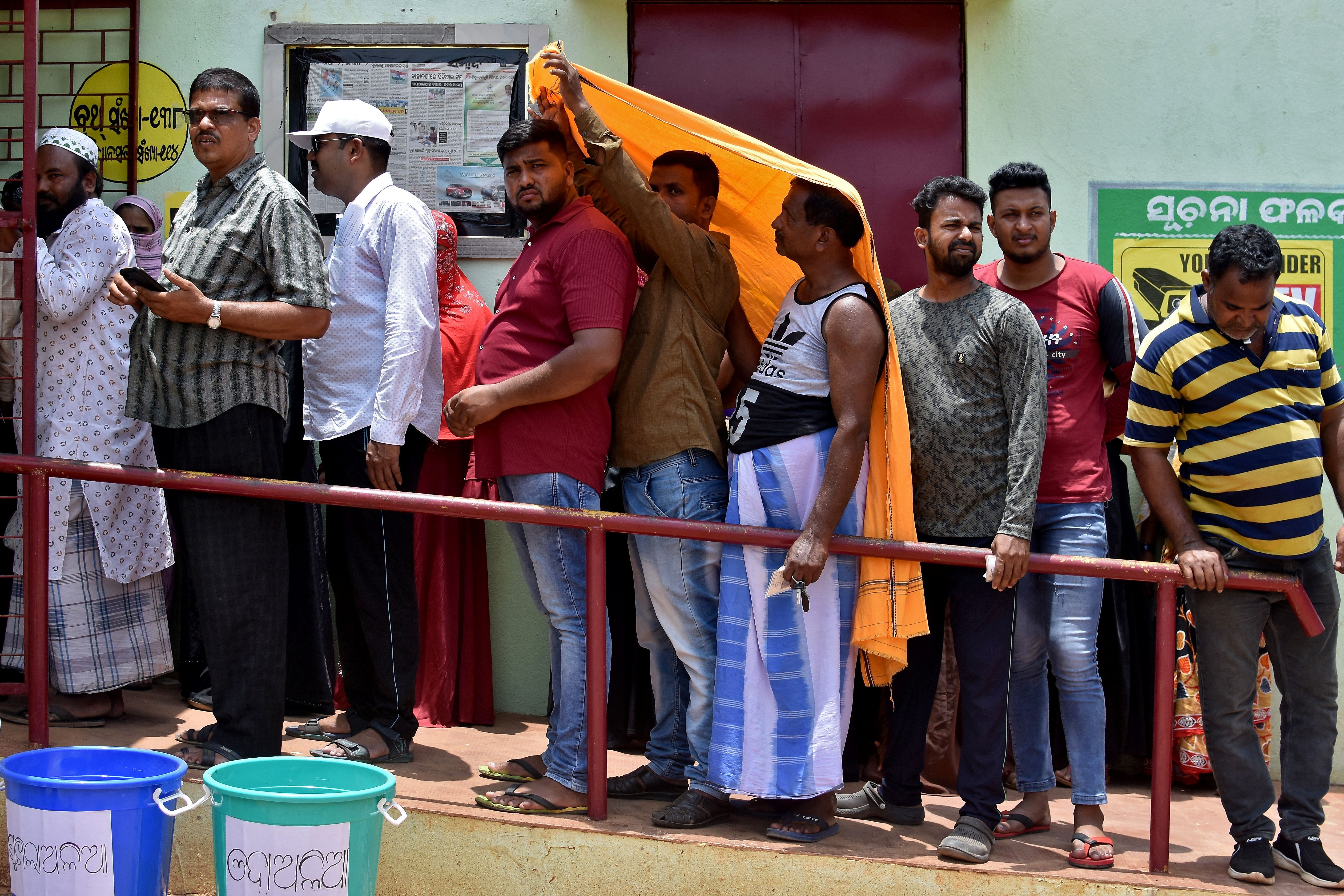 Men use a stole to cover from heat as they wait in a line outside a polling station to cast their votes during the sixth phase of India’s general election, on a hot summer day in Bhubaneswar, India, May 25, 2024.