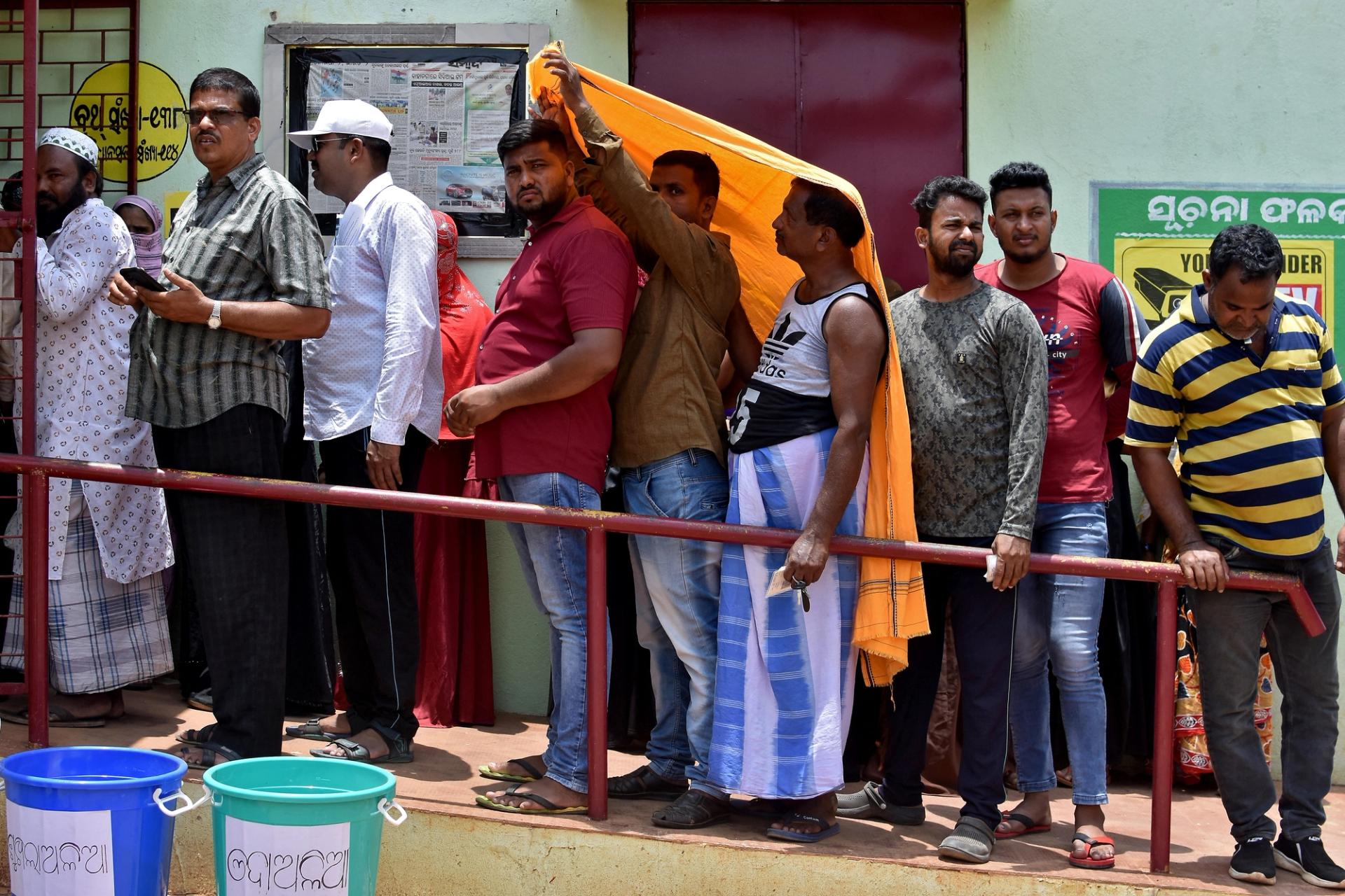 Men use a stole to cover from heat as they wait in a line outside a polling station to cast their votes during the sixth phase of India's general election, on a hot summer day in Bhubaneswar, India, May 25, 2024.