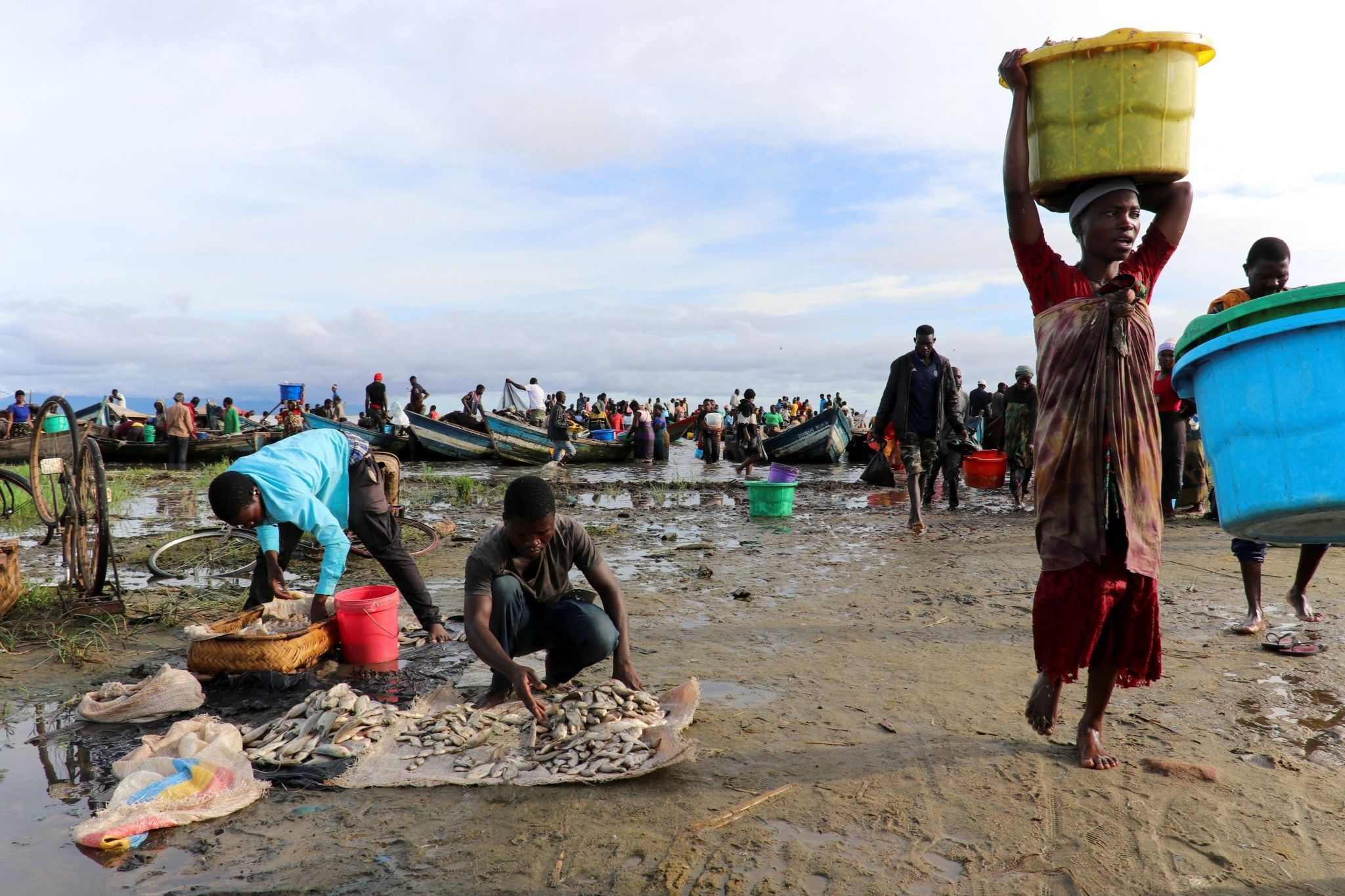 A woman carries a fish basket as she walks past fishermen sorting their catch on the shores of Lake Chilwa, near the border with Mozambique, in Malawi