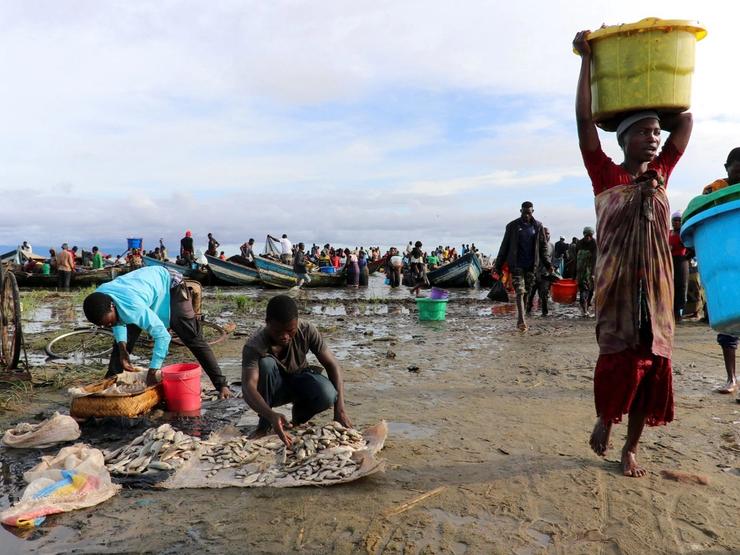 A woman carries a fish basket as she walks past fishermen sorting their catch on the shores of Lake Chilwa, near the border with Mozambique, in Malawi