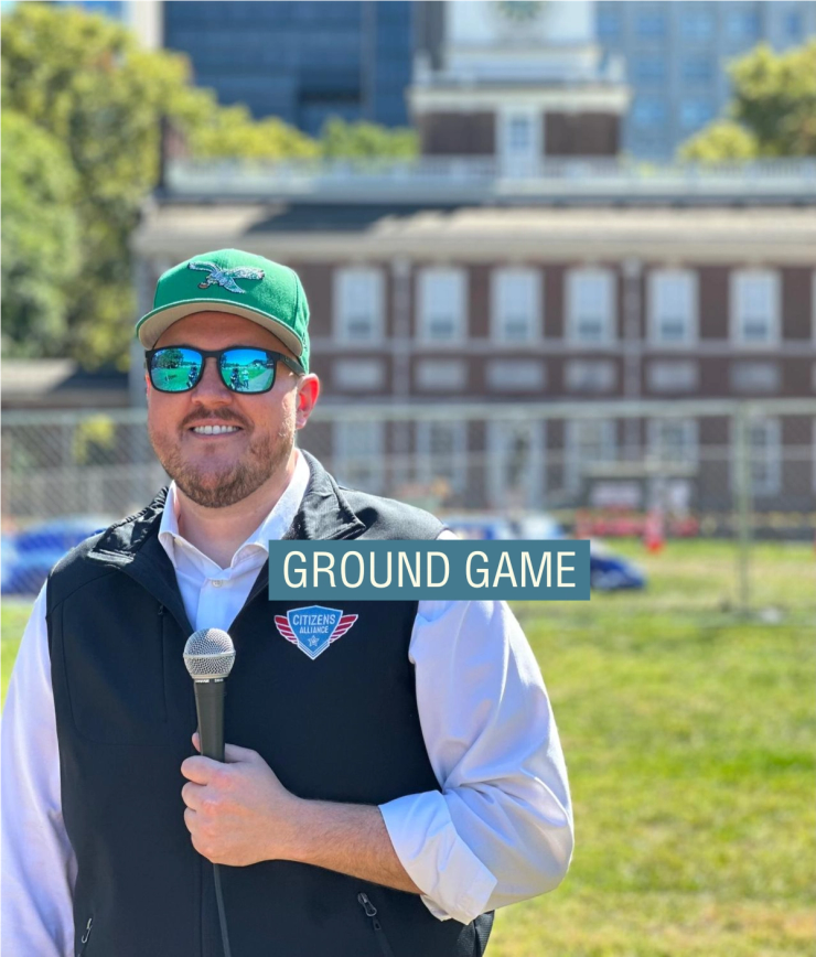 Cliff Maloney, a white, bearded man wearing a hat and holding a microphone.