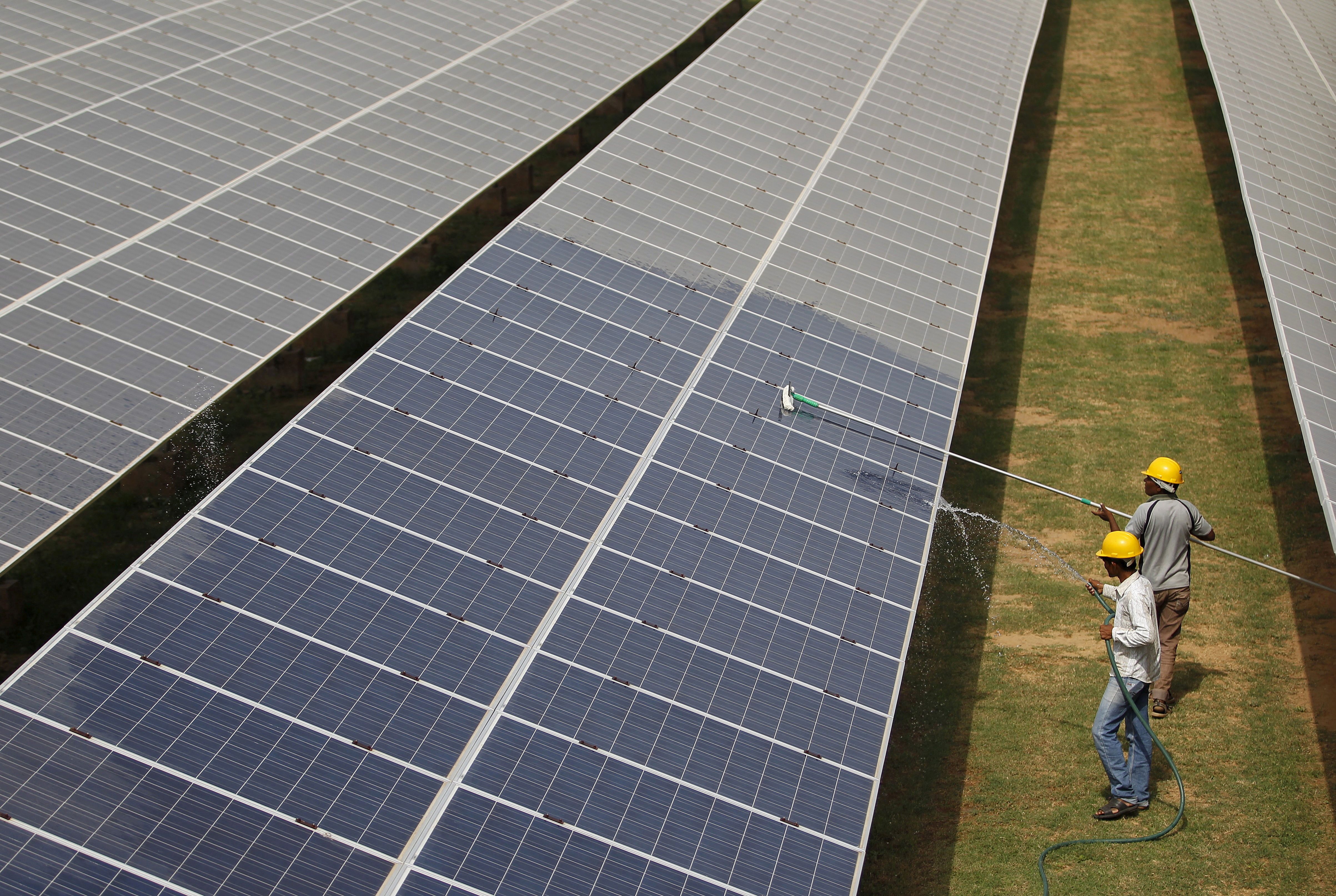 Workers clean photovoltaic panels inside a solar power plant in Gujarat