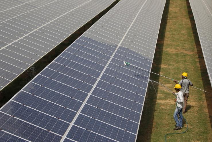 Workers clean photovoltaic panels inside a solar power plant in Gujarat