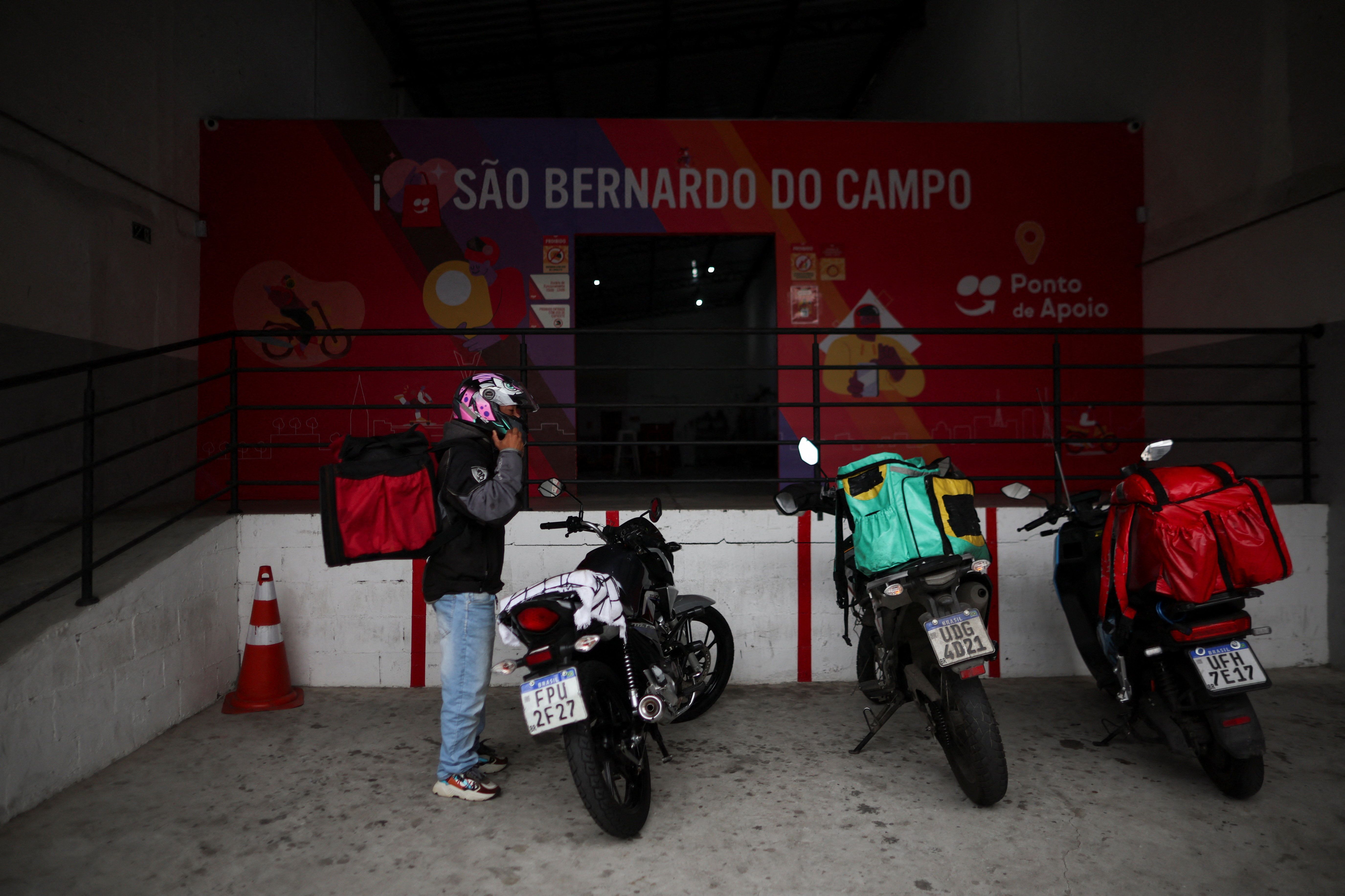 An app delivery driver stands next to his motorcycle in Brazil. 