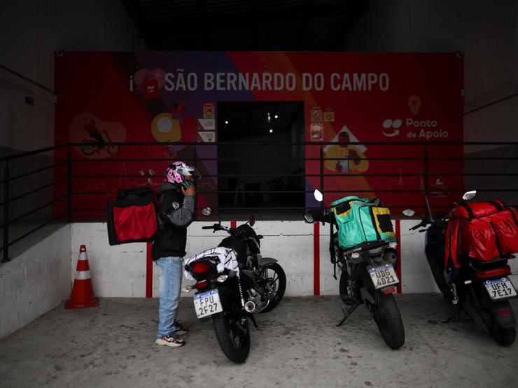 An app delivery driver stands next to his motorcycle in Brazil.