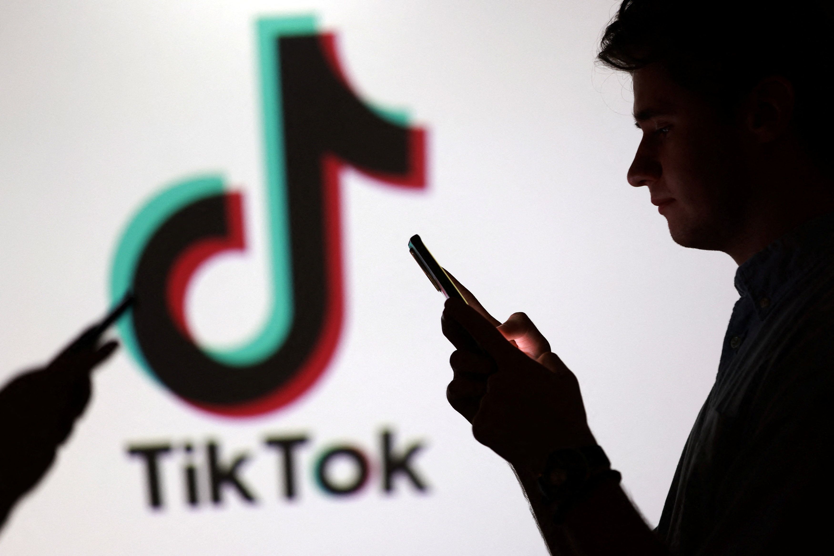 Illustration shows teenagers pose for a photo while holding smartphones in front of a TikTok logo.