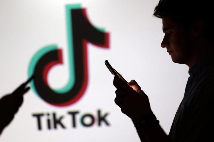 Illustration shows teenagers pose for a photo while holding smartphones in front of a TikTok logo.