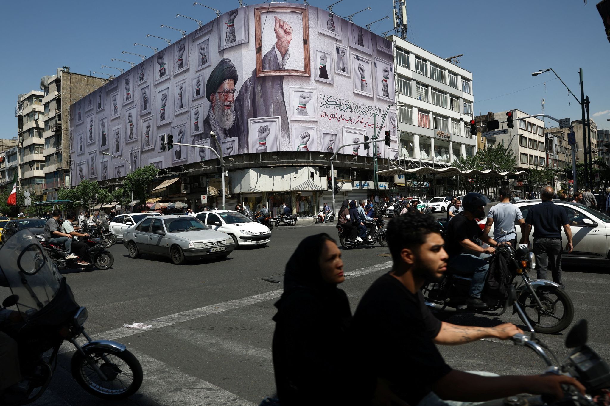 People ride motorcycles near a billboard featuring an image of the late Supreme Leader of Iran, Ayatollah Ali Khamenei, in Tehran