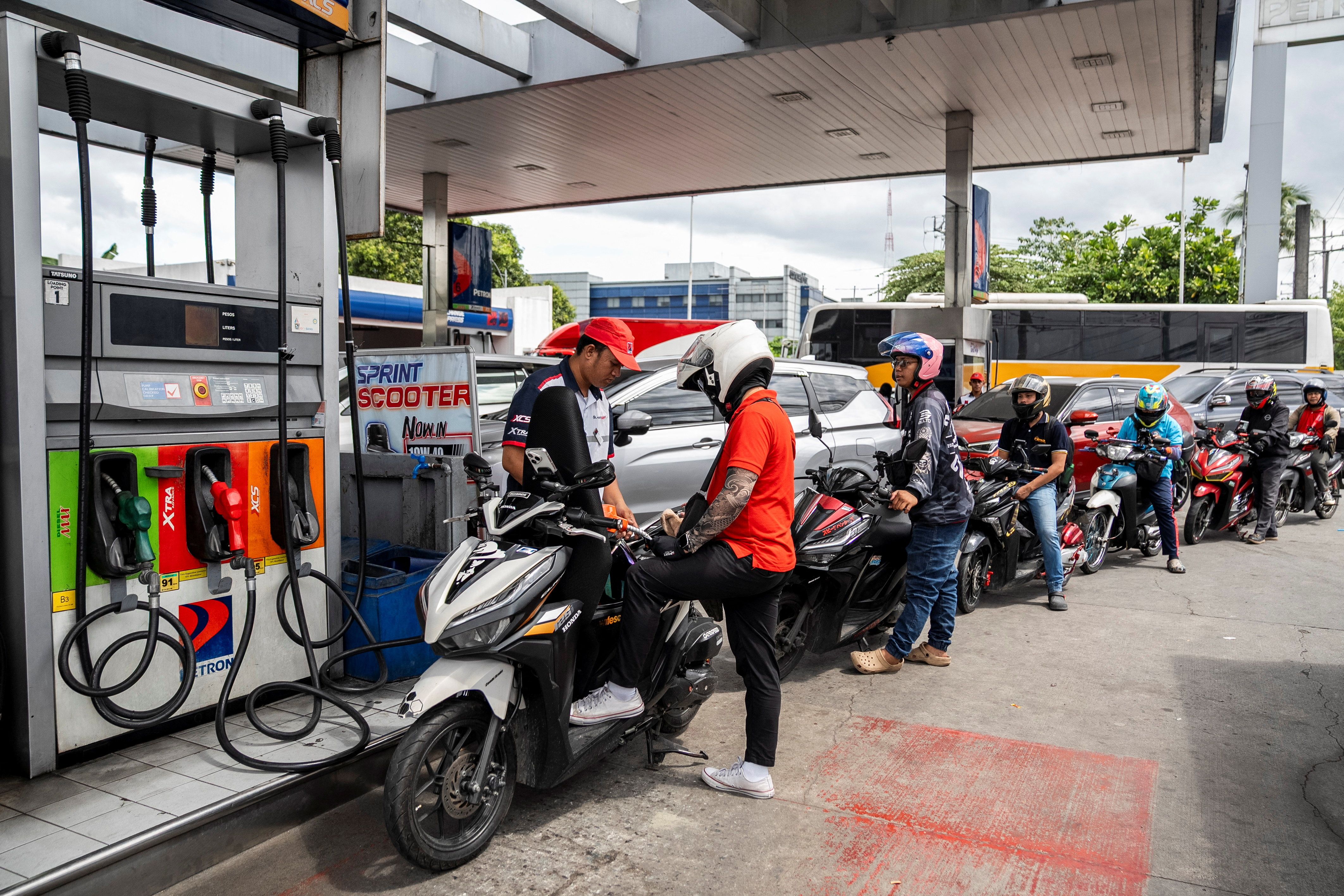 A worker fills up a motorcycle while drivers queue at a gas station in Manila.