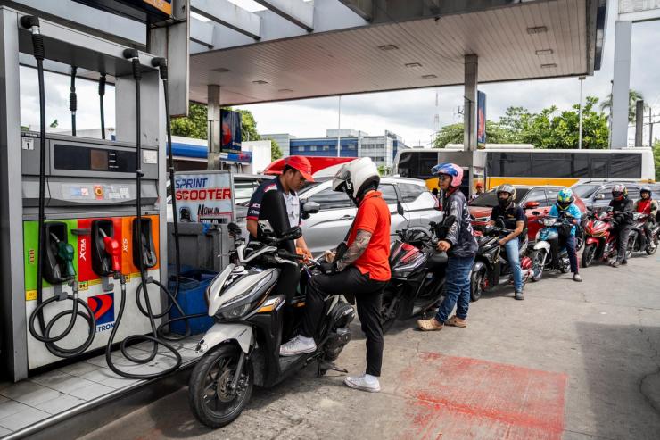 A worker fills up a motorcycle while drivers queue at a gas station in Manila.