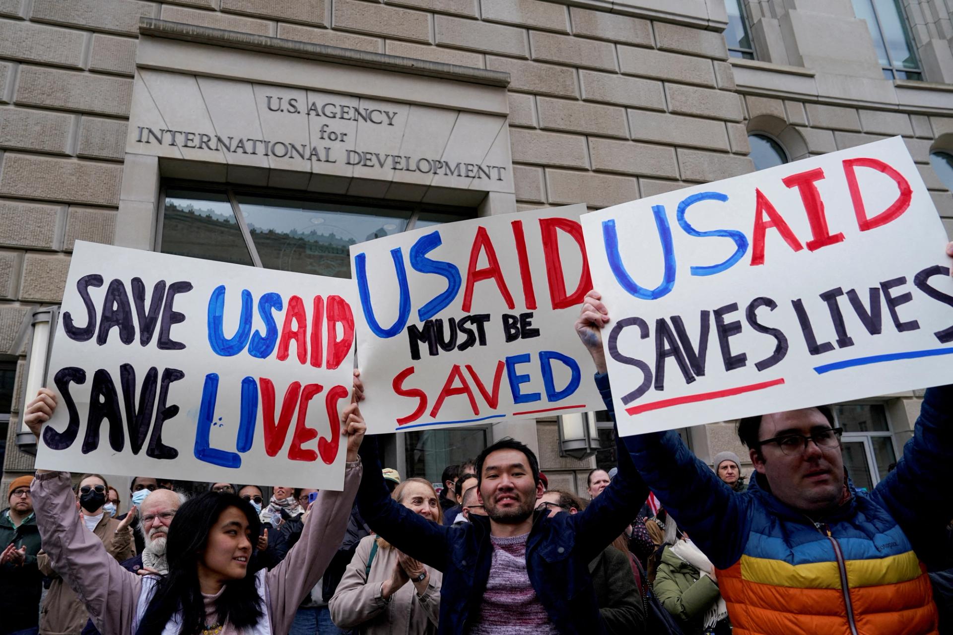 People hold placards, as the USAID building sits closed.