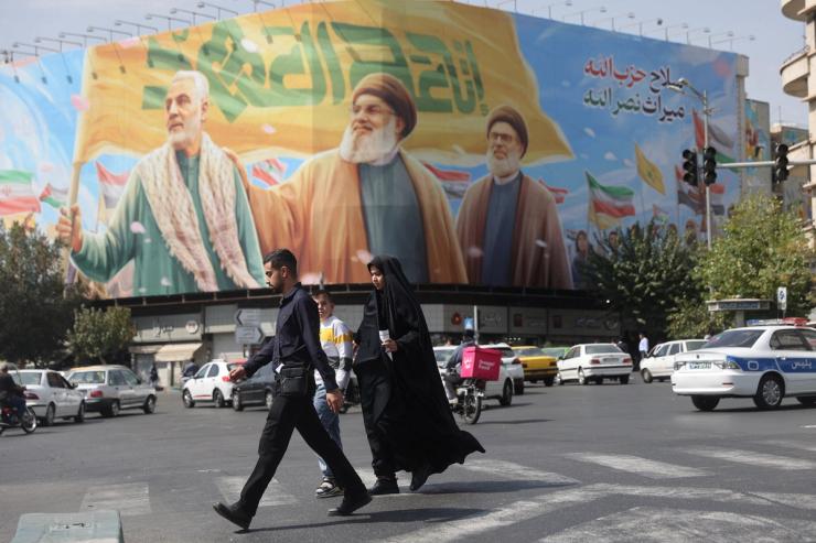 People walk past a billboard with a picture of late Hezbollah leaders Hassan Nasrallah and Hashem Safieddine and senior Iranian military commander General Qassem Soleimani