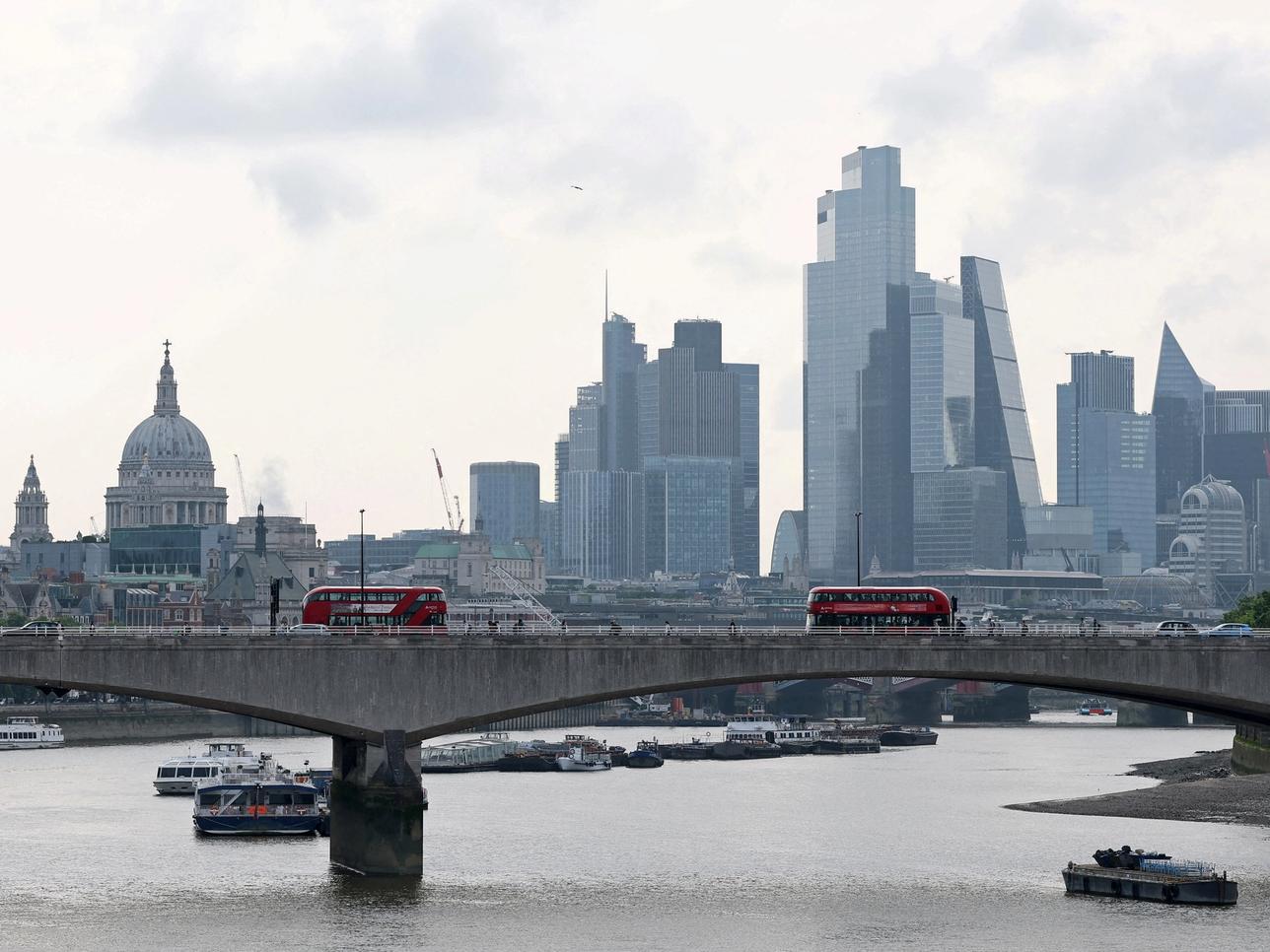 London buses cross Waterloo Bridge with St. Paul’s Cathedral and skyscrapers of the City of London business district seen behind.