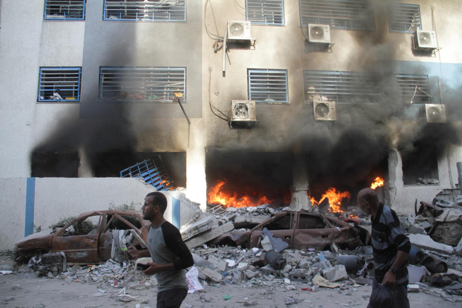 Palestinians walk next to a fire at a school sheltering displaced people, after it was hit by an Israeli strike, in Gaza City