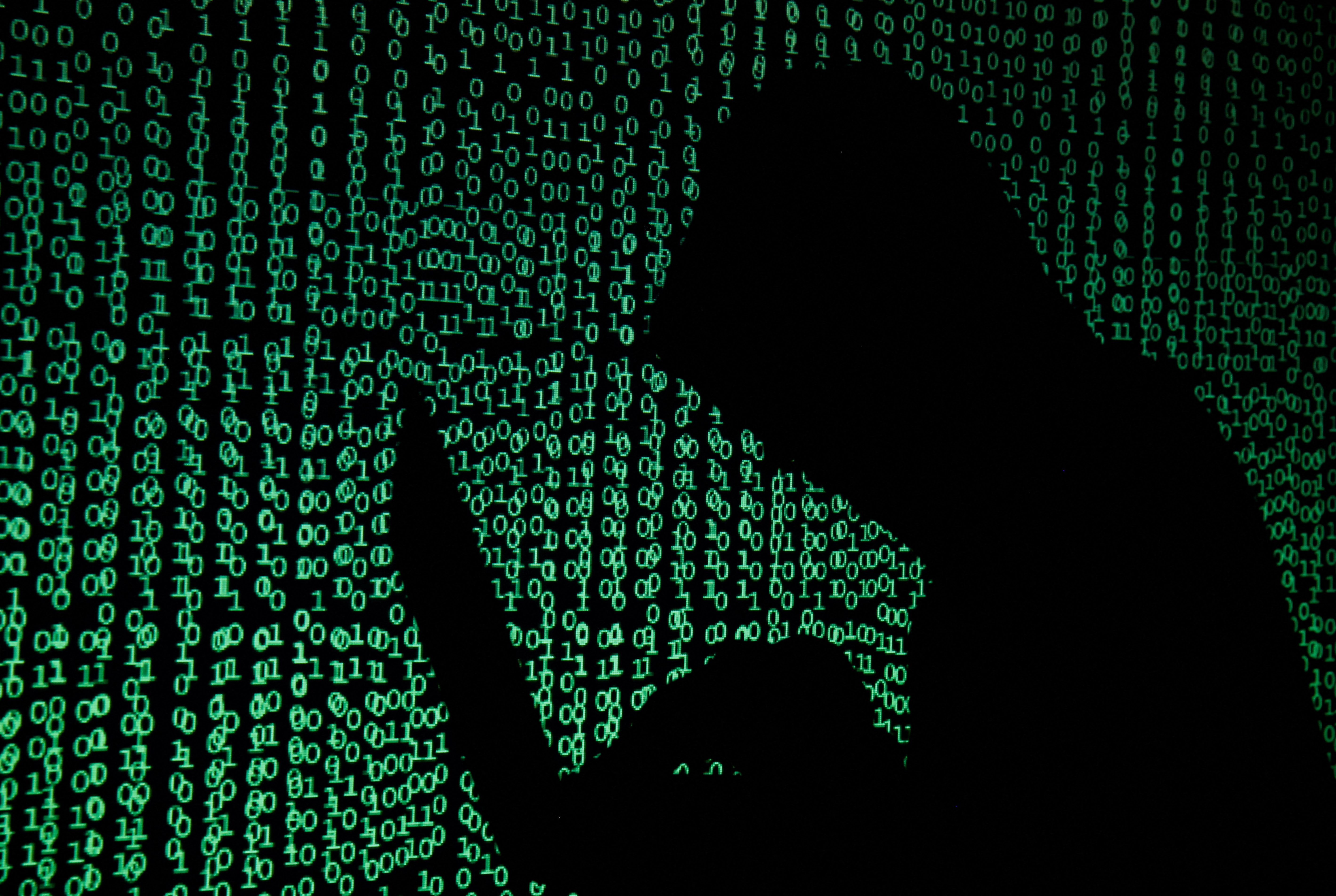 A hooded man holds a laptop computer as cyber code is projected on him.