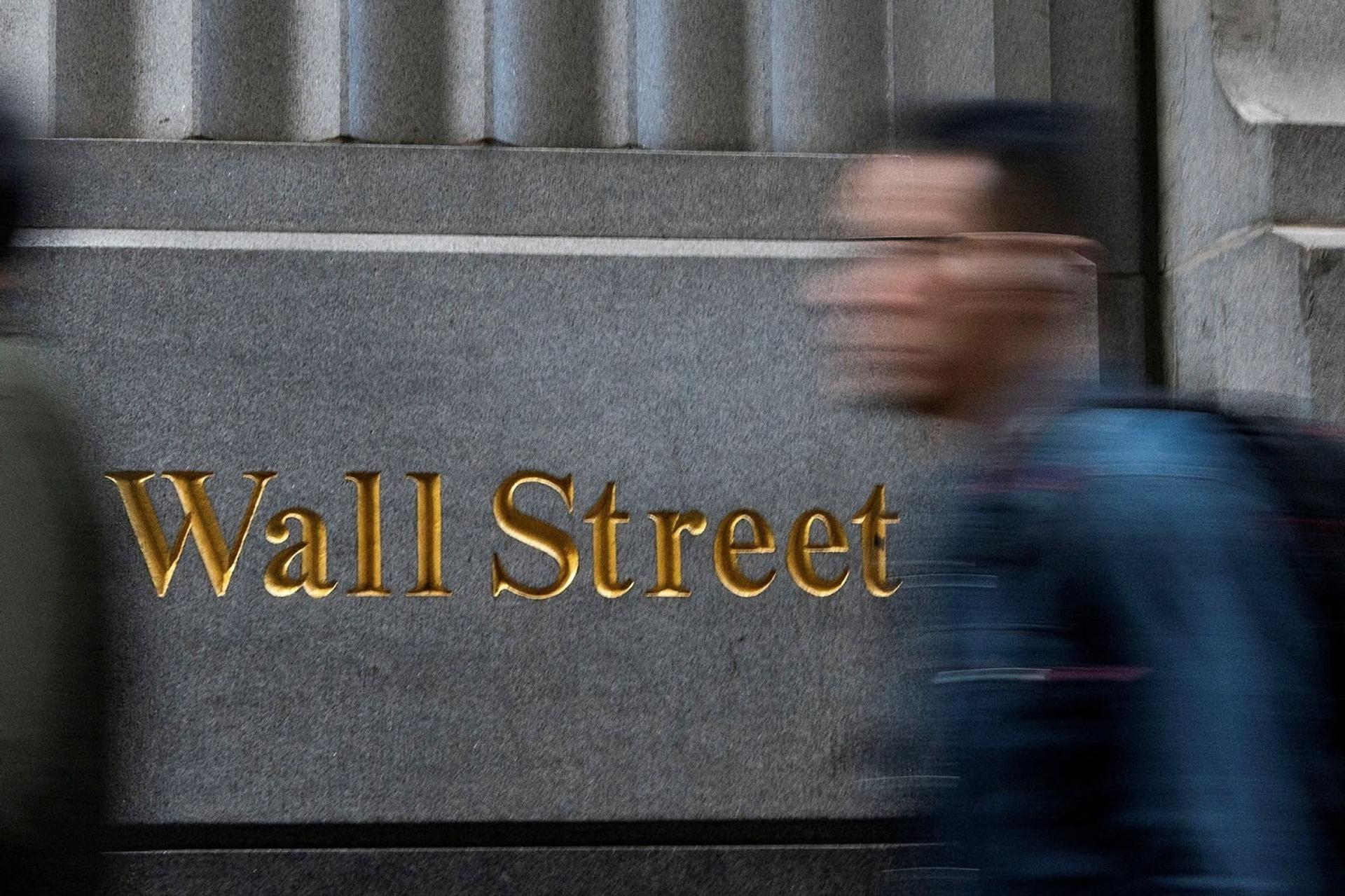 A person walks past a sign that says “Wall Street” near the New York Stock Exchange