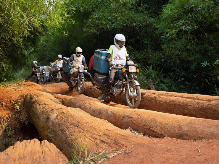 A motorcycle convoy carrying vials of measles vaccine and other supplies for medial NGO Doctors Without Borders (MSF) crosses a log bridge.
