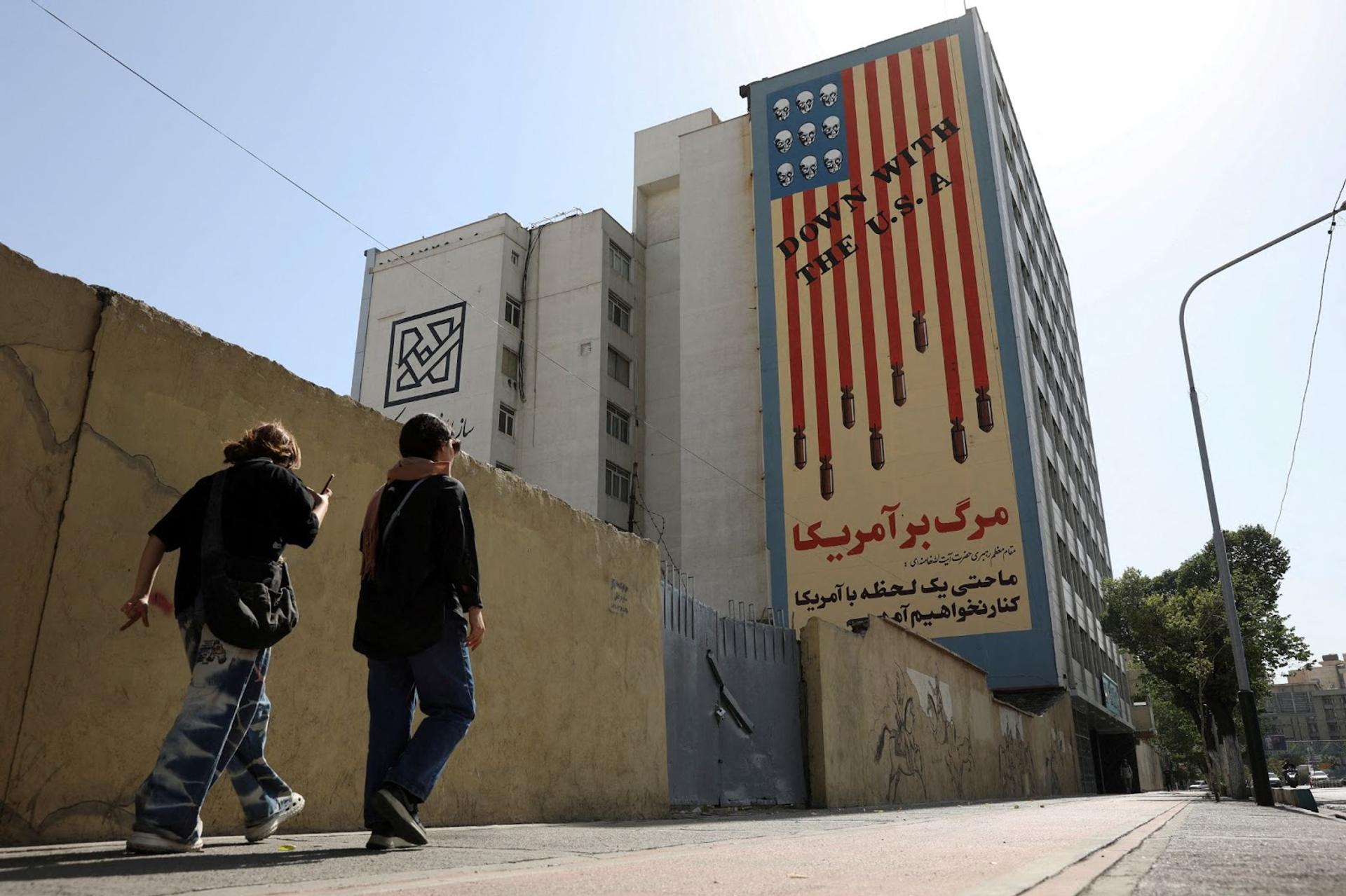 People walk past an anti-US mural on a street in Tehran