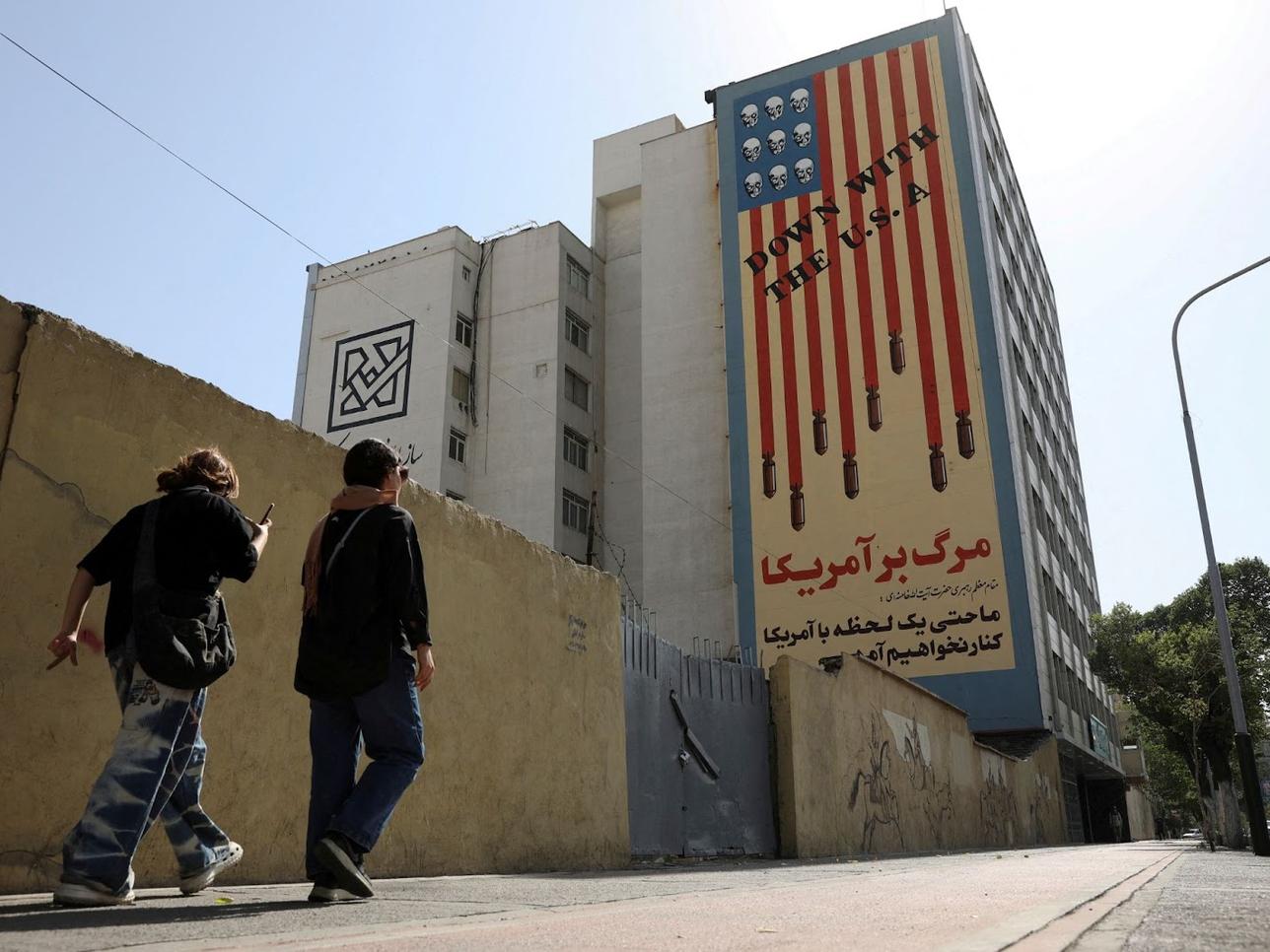People walk past an anti-US mural on a street in Tehran
