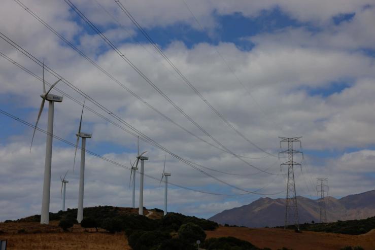 Wind turbines spin next to power lines connecting pylons of high-tension electricity, near Casares, Spain.