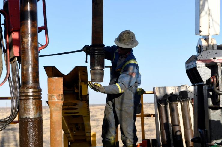 An oil worker removes a thread cap from a piece of drill pipe on a drilling lease owned by Elevation Resources near Midland, Texas, U.S.