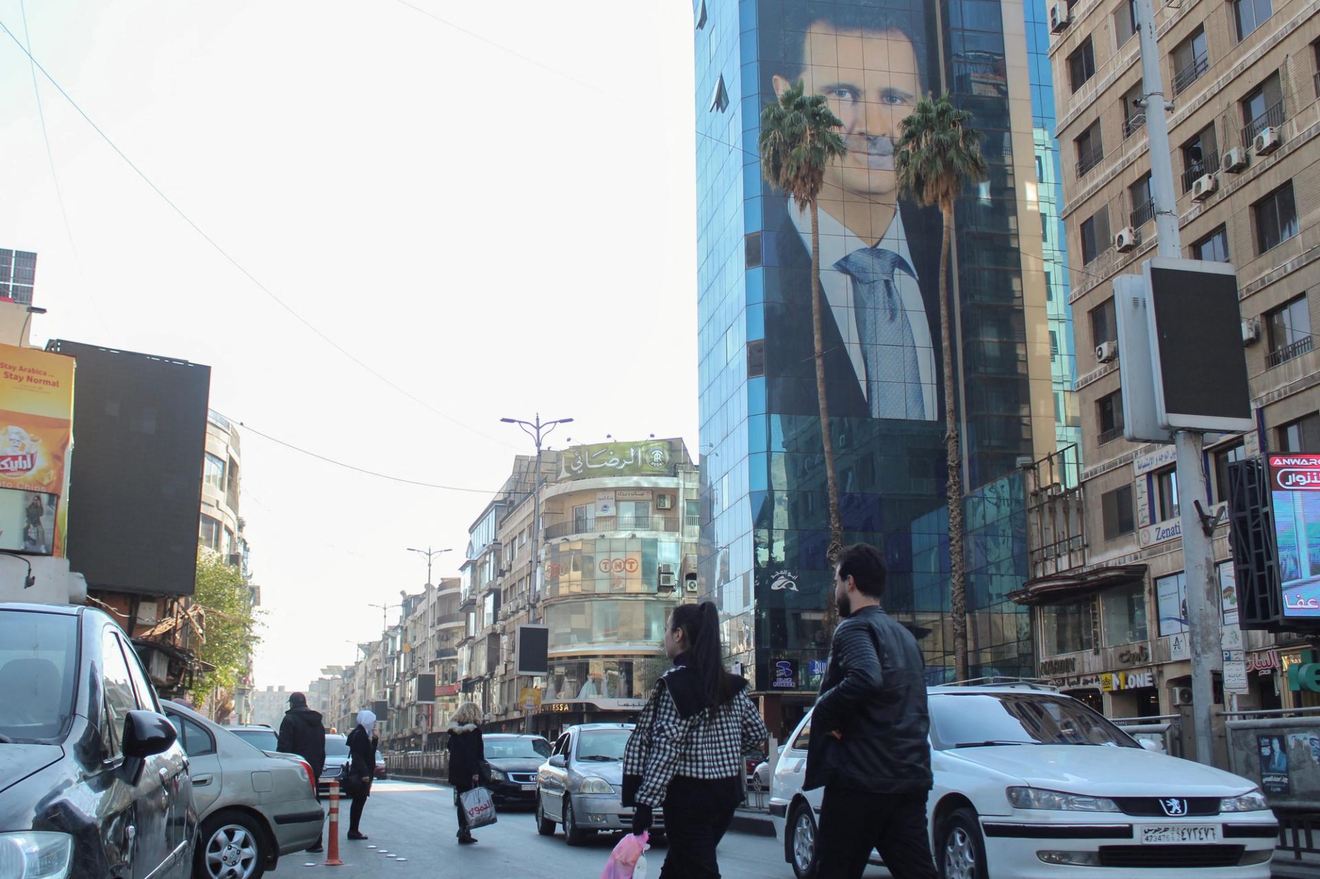 People walk past a poster depicting Bashar al-Assad in Damascus