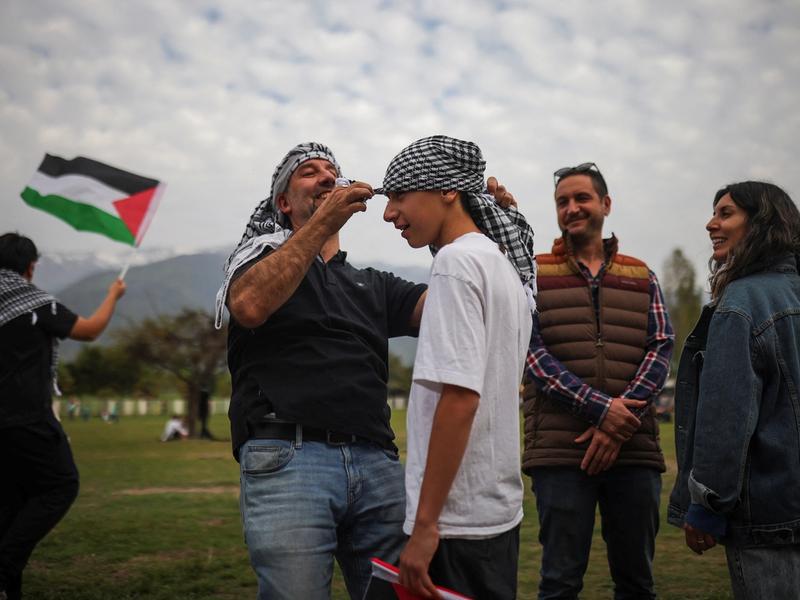 A pro-Palestinian activist helps a man put on a Palestinian keffiyeh before a charity concert to fund hospitals in Gaza and West Bank, in Santiago, Chile October 25, 2023.