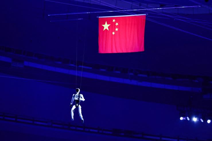 A humanoid robot walks in the air while on strings near a Chinese national flag during the opening ceremony of the World Humanoid Robot Games 2026 at the National Speed Skating Oval stadium, in Beijing,