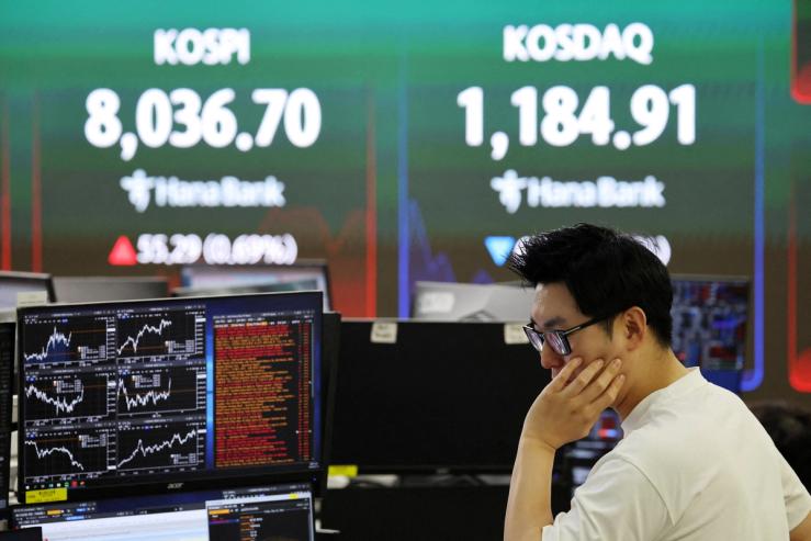 A currency dealer works as an electronic board displays the Korea Composite Stock Price Index (KOSPI) and the Korea Securities Dealers Automated Quotations (KOSDAQ).