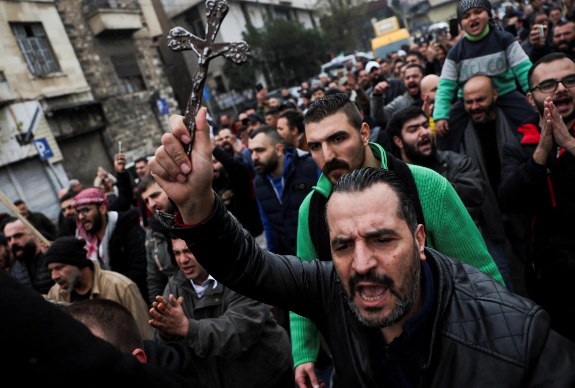 A man carries a cross at a protest against the burning of a Christmas tree in Damascus