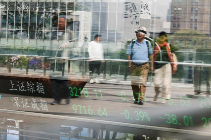 An electronic board shows Shanghai and Shenzhen stock indices as people walk on a pedestrian bridge at the Lujiazui financial district in Shanghai, China.