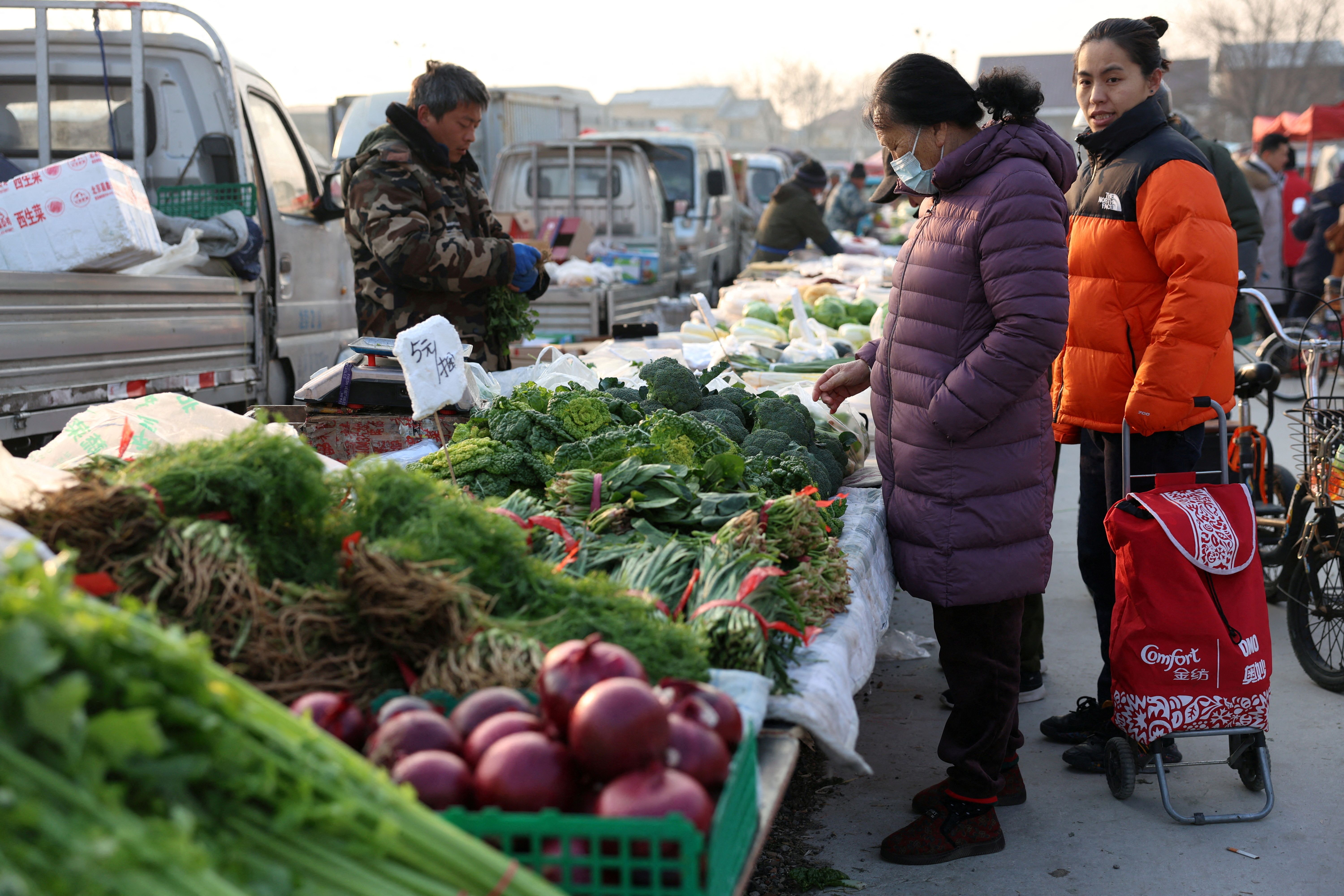 A woman looks at vegetables displayed at a stall at an outdoor market in Beijing, China.