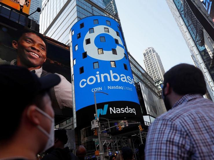 People watch as the logo for Coinbase Global Inc, is displayed on the Nasdaq MarketSite jumbotron in Times Square.