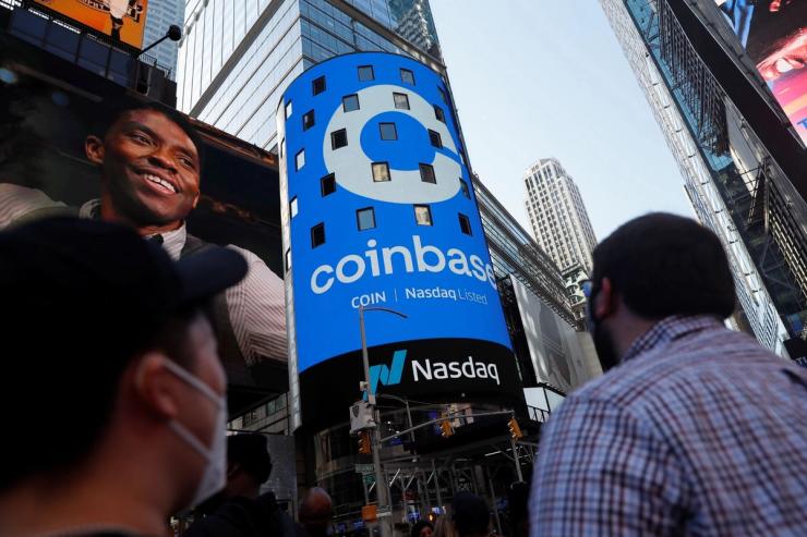 People watch as the logo for Coinbase Global Inc, is displayed on the Nasdaq MarketSite jumbotron in Times Square.