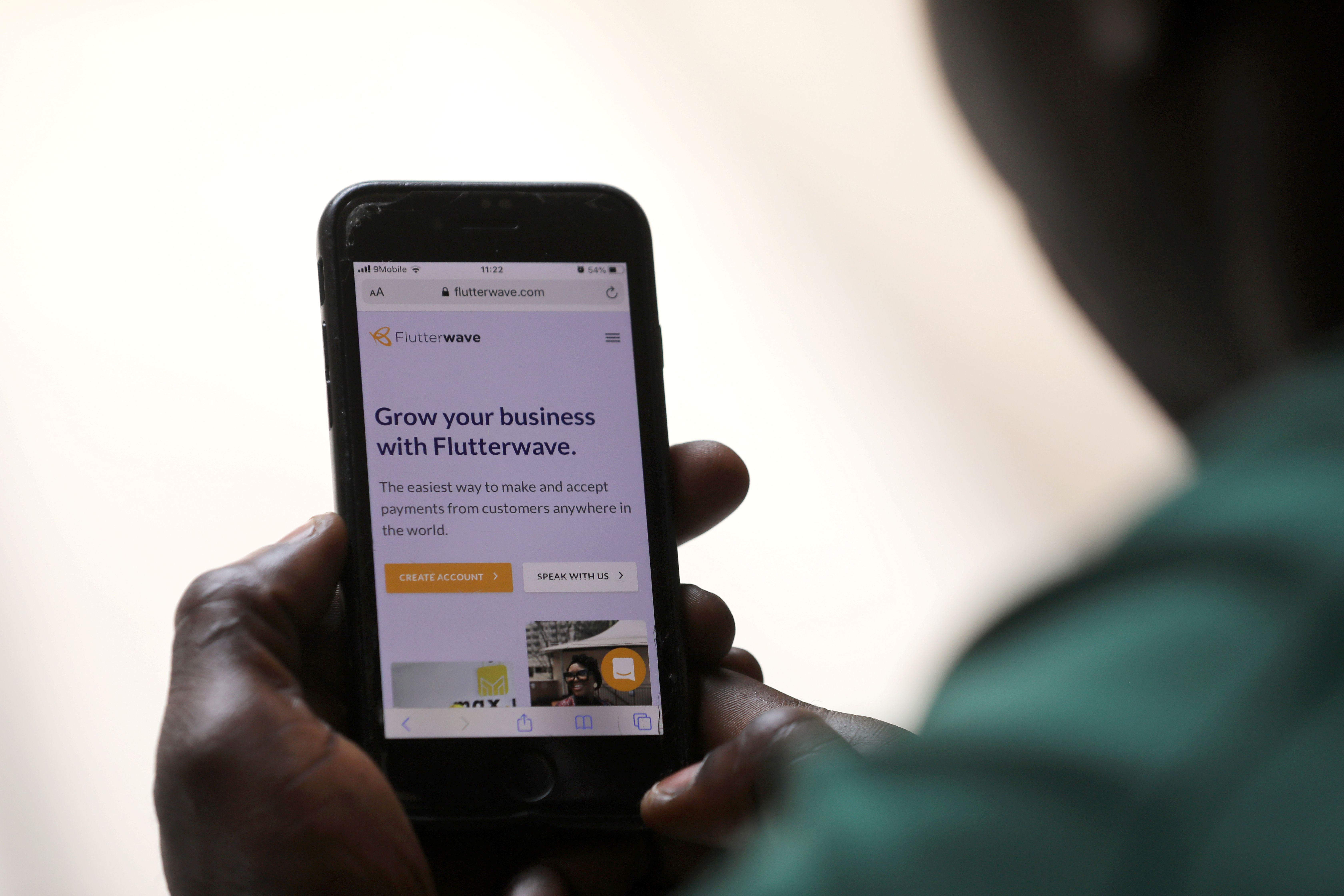Man poses as he displays Flutterwave homepage on mobile phone screen in Abuja.