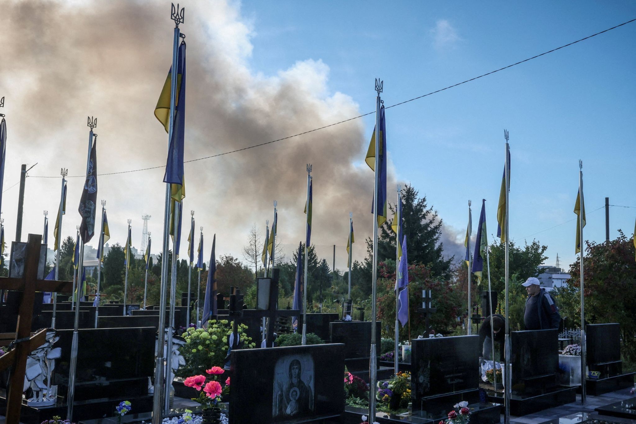 Smoke from a Russian drone strike rises behind the graves of soldiers in Ukraine.