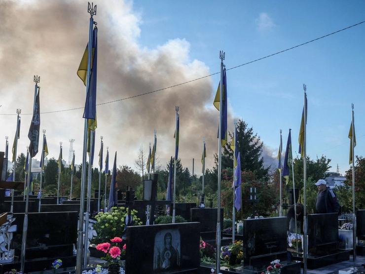 Smoke from a Russian drone strike rises behind the graves of soldiers in Ukraine.