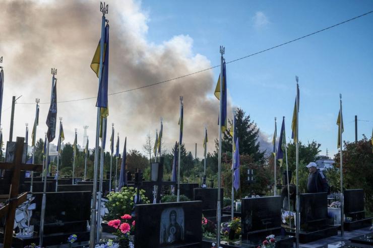 Smoke from a Russian drone strike rises behind the graves of soldiers in Ukraine.