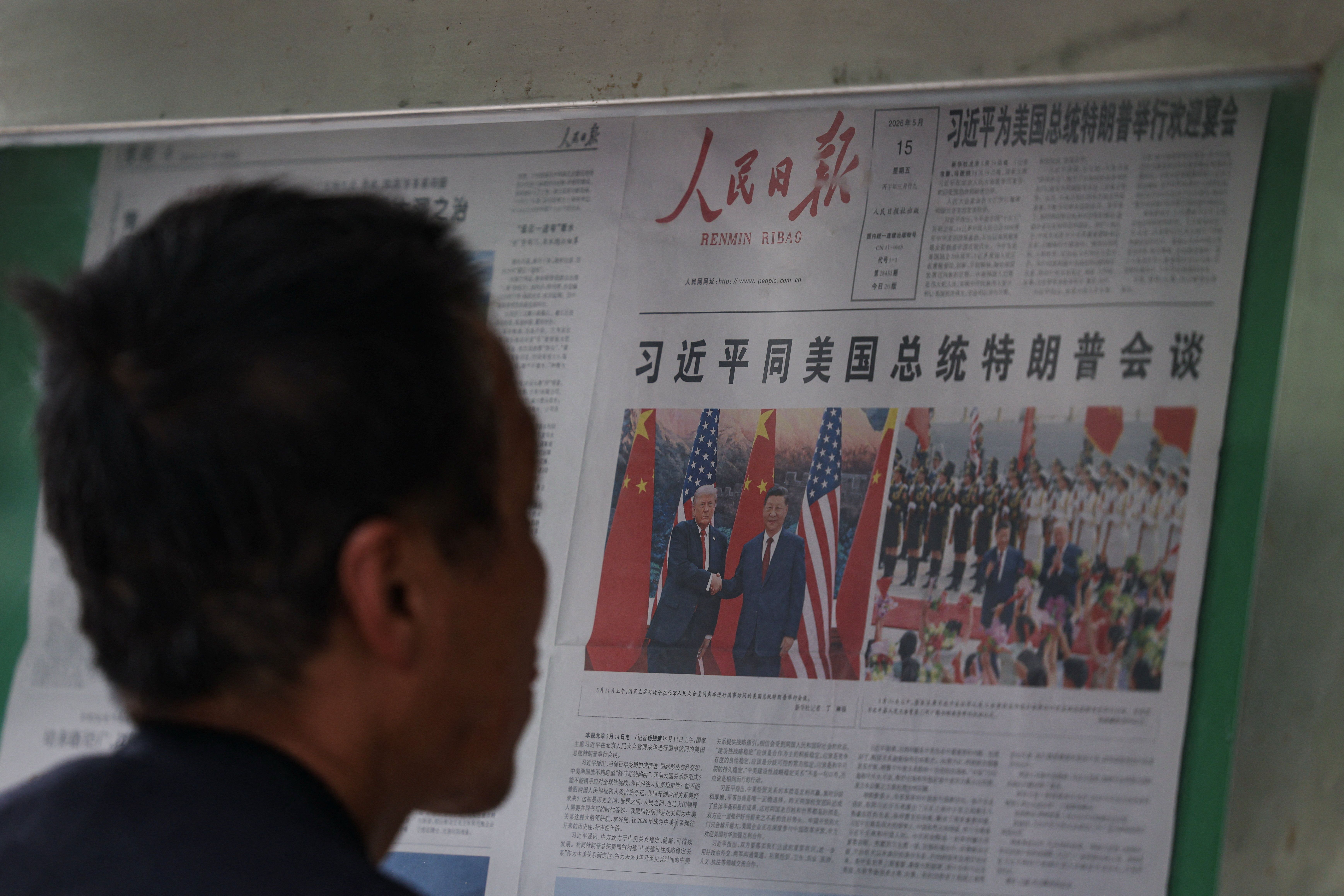 A man reading a newspaper with Trump and Xi. 