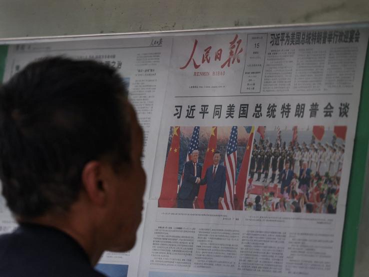 A man reading a newspaper with Trump and Xi.