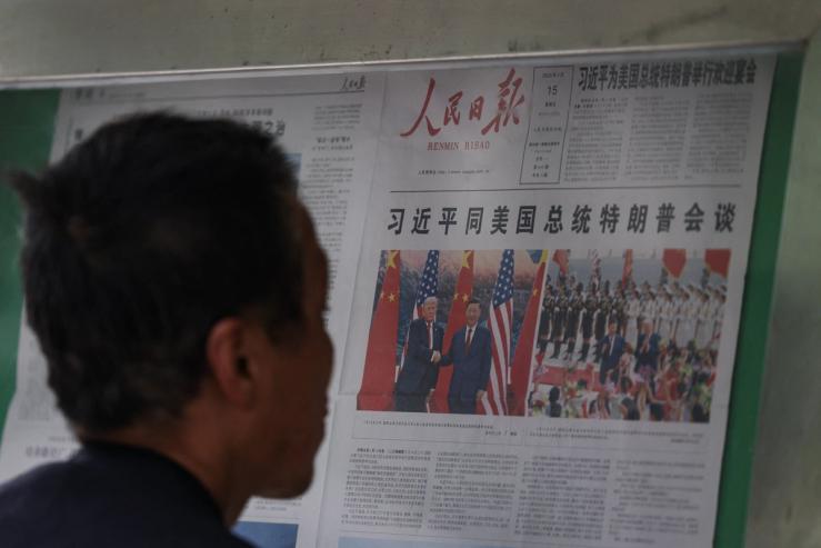 A man reading a newspaper with Trump and Xi.
