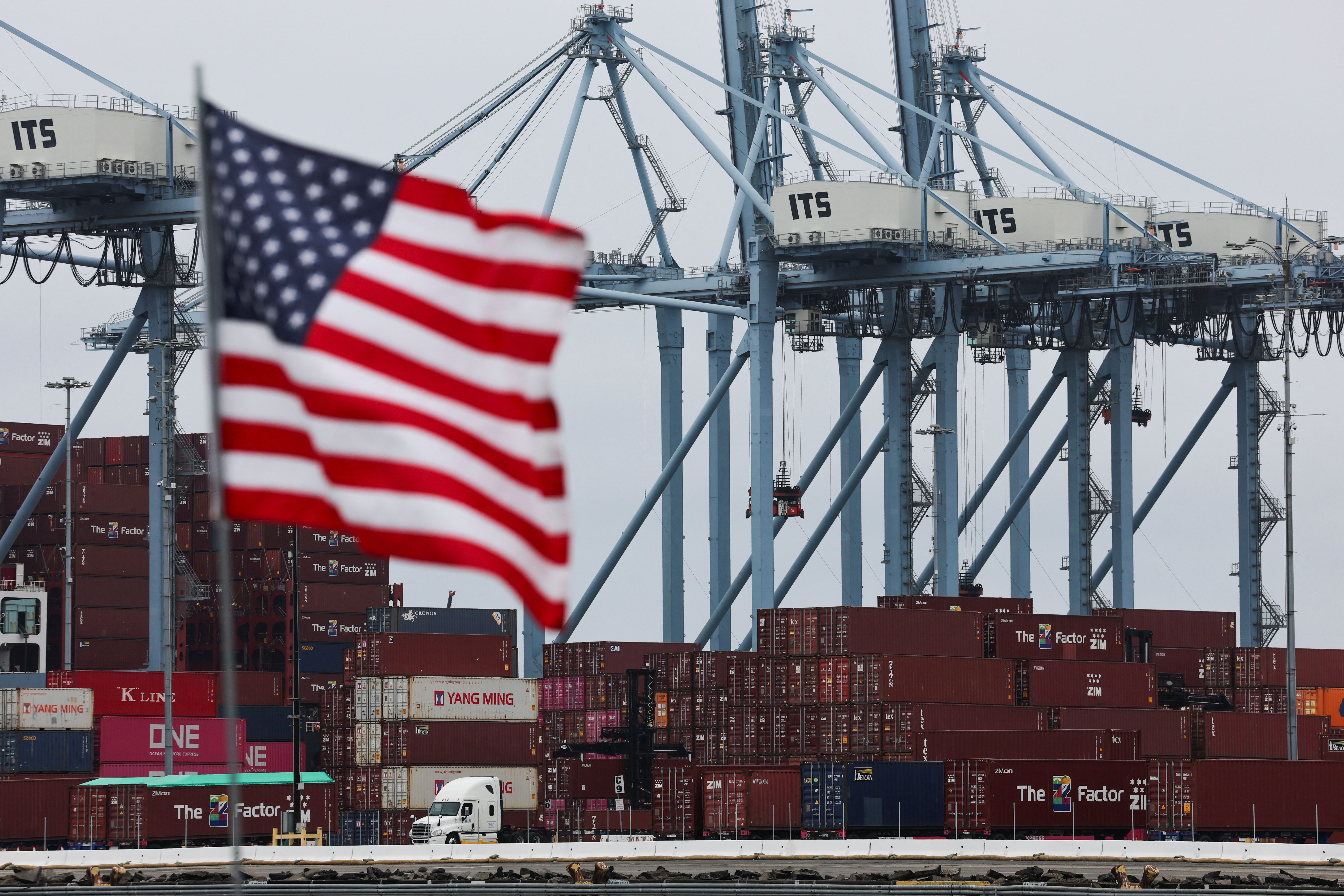 A U.S. flag flutters in front of shipping containers at the Port of Long Beach in Long Beach, California, U.S., July 11, 2025. 