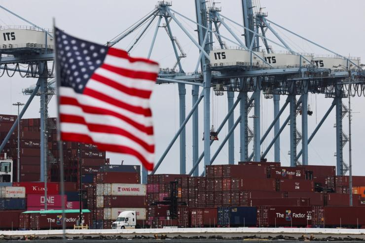 A U.S. flag flutters in front of shipping containers at the Port of Long Beach in Long Beach, California, U.S., July 11, 2025.