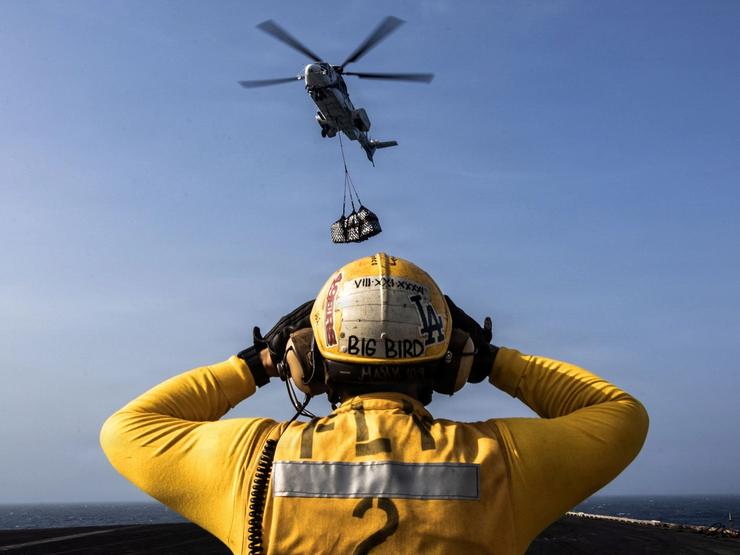A US Navy sailor directs a Eurocopter AS-332 Super Puma helicopter on a US aircraft carrier